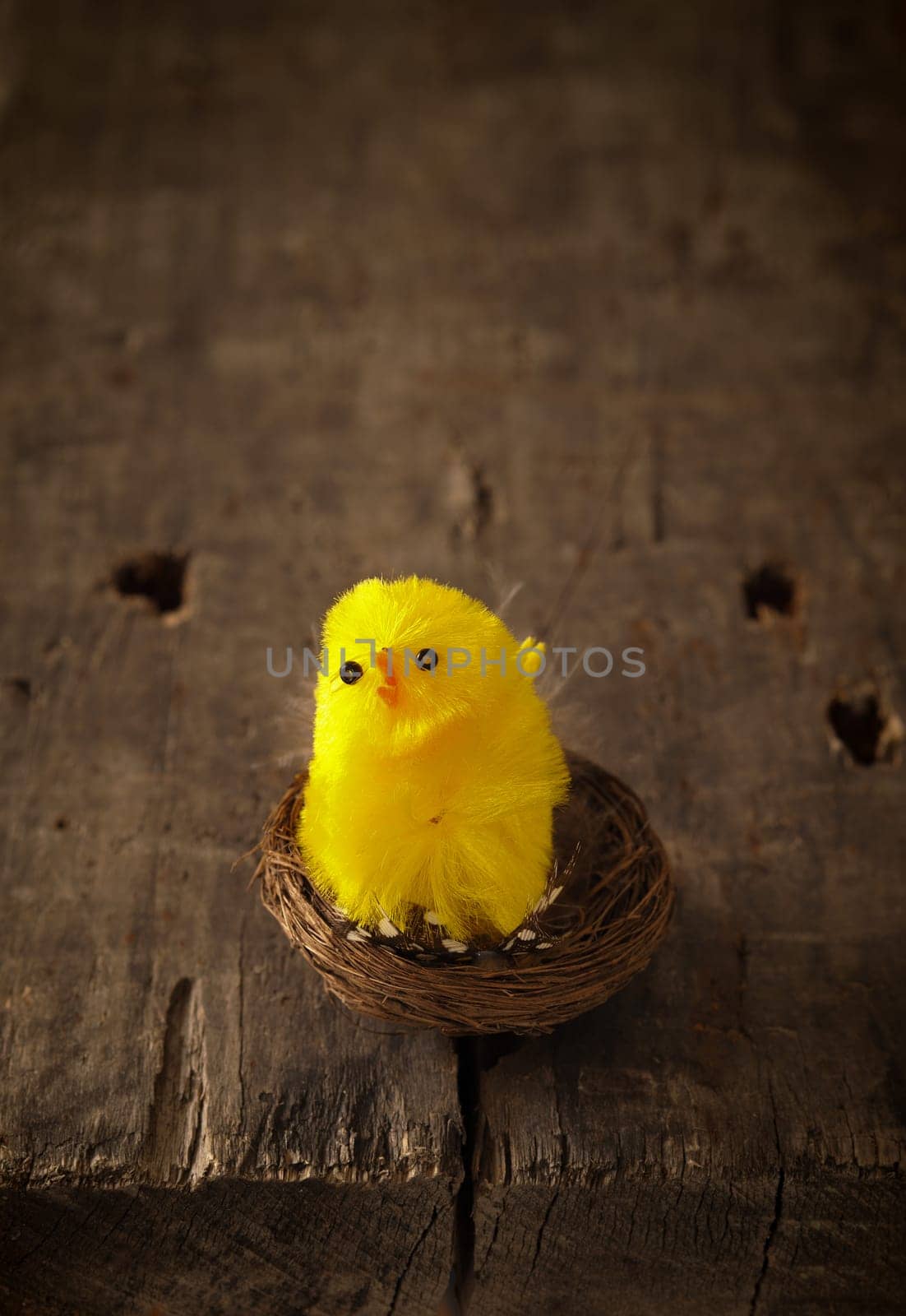 Cute little chicken decoration in a nest on a rustic wooden table, Easter or spring background