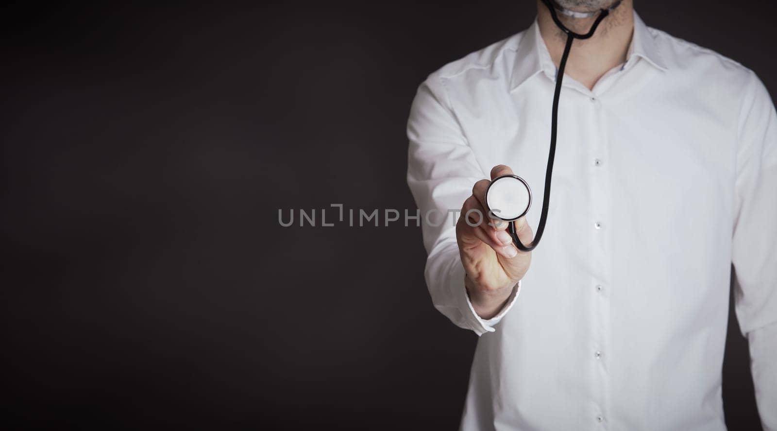 Hand of a doctor with a stethoscope on a dark background with space for text or image, selective focus on foreground