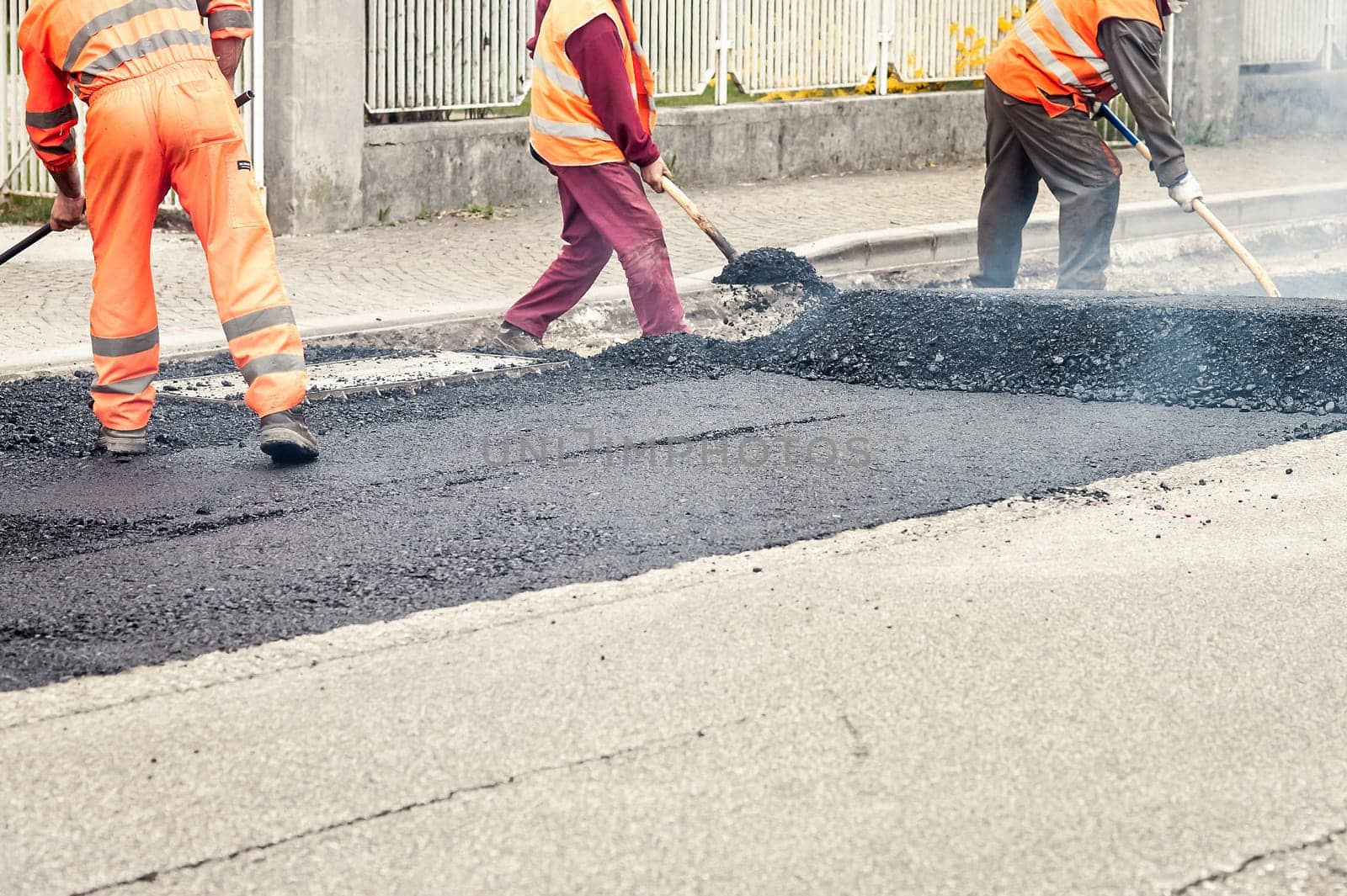 Construction workers during asphalting road works wearing coveralls. Manual labor on construction site.