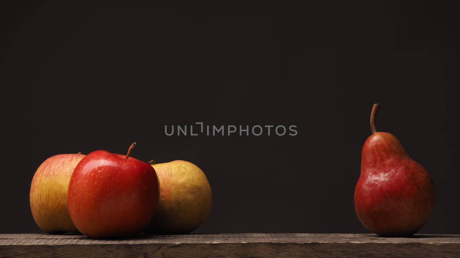 Three apples and one pear on a rustic wooden table, using as background with space for text