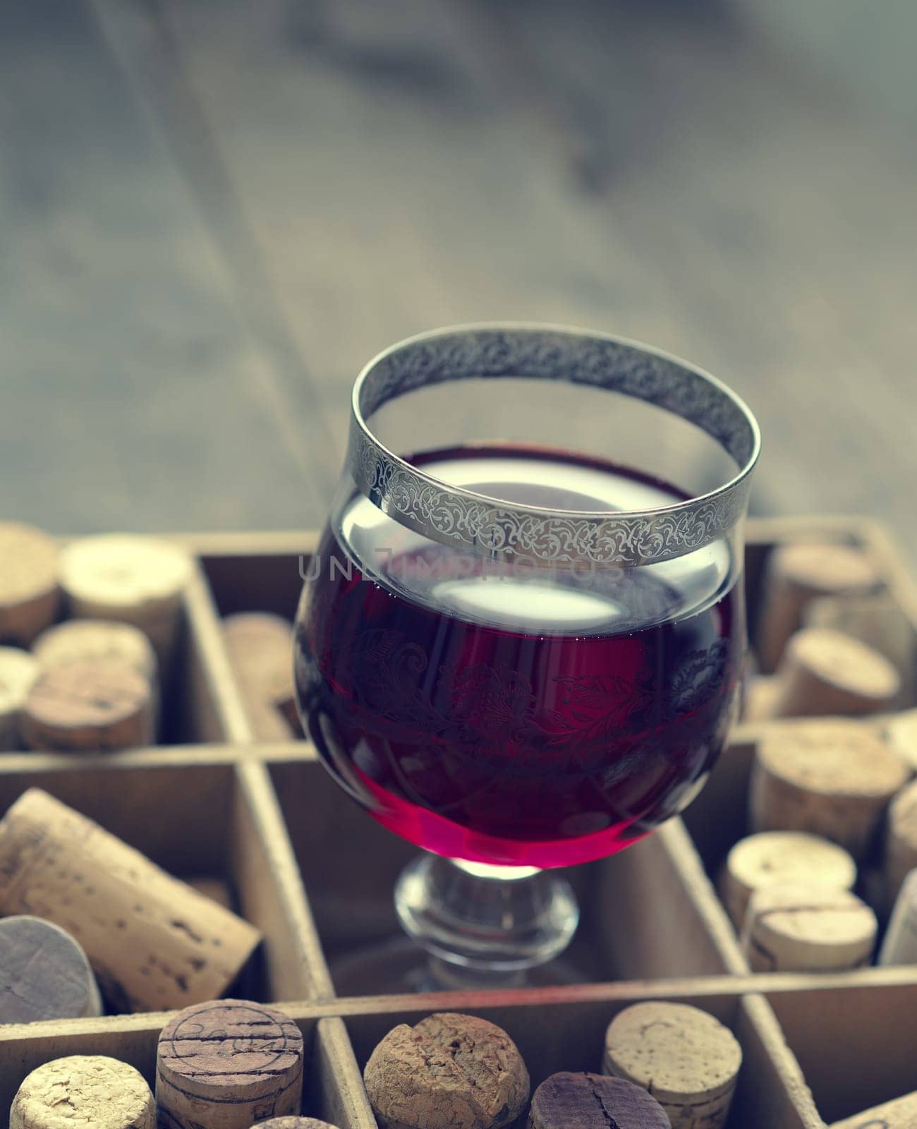 Glass of red wine in a wooden box with bottle cork, vintage color toned