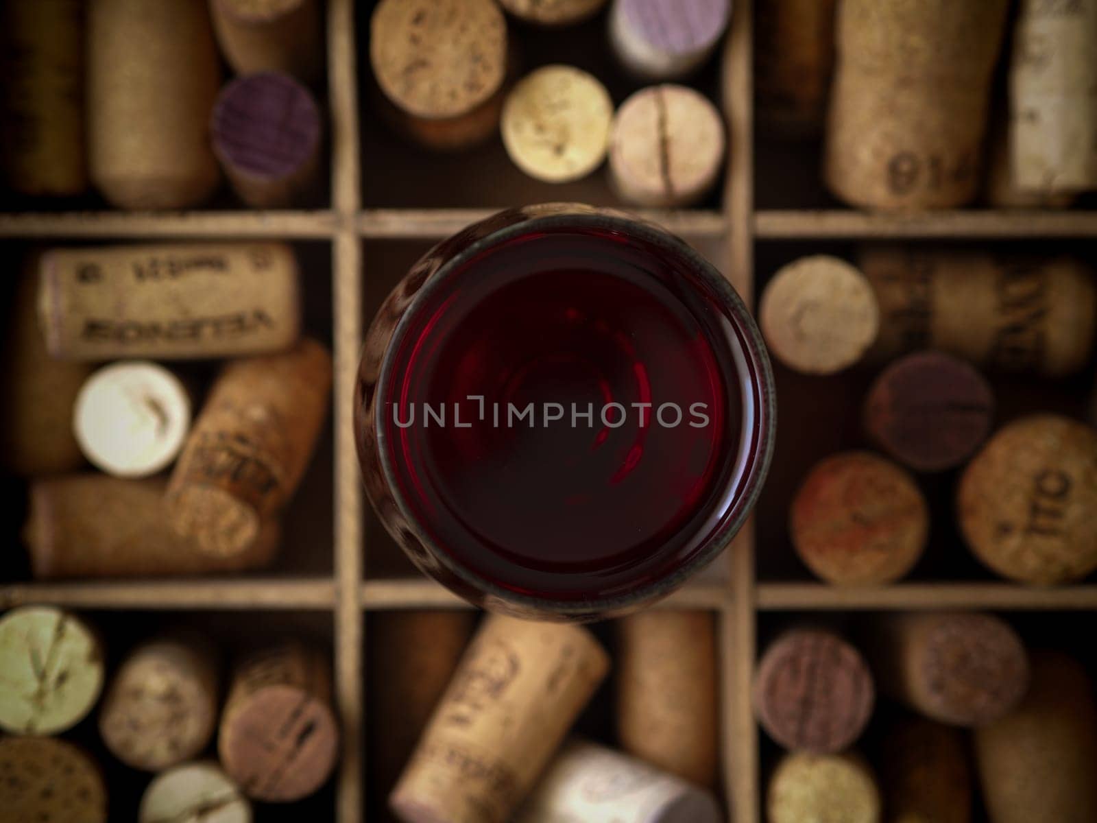 Glass of red wine on bottle corks in a wooden box, view from above