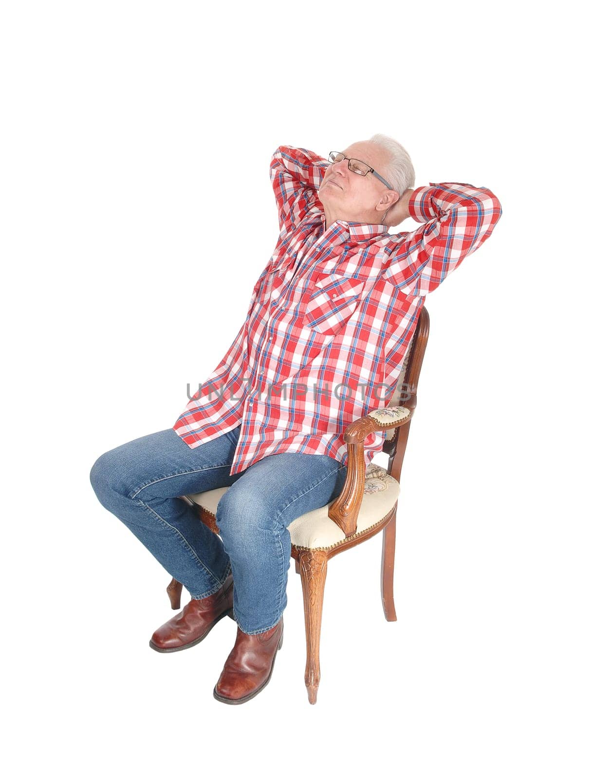 An senior citizen man in a checkered shirt and jeans sitting on a chair.with his hands behind his head, isolated for white background..