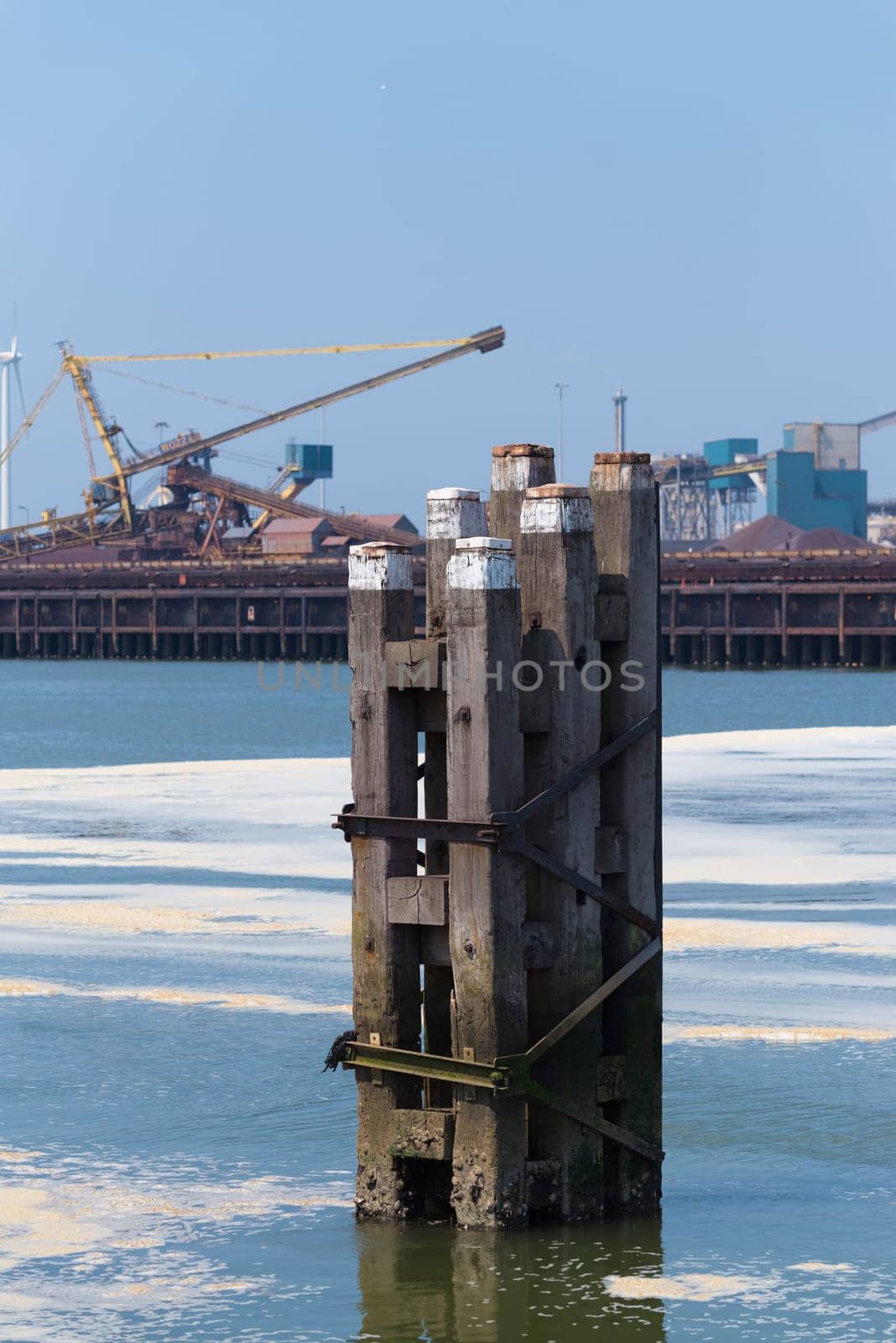 wooden poles that mark the waterway in front of a large steel plant