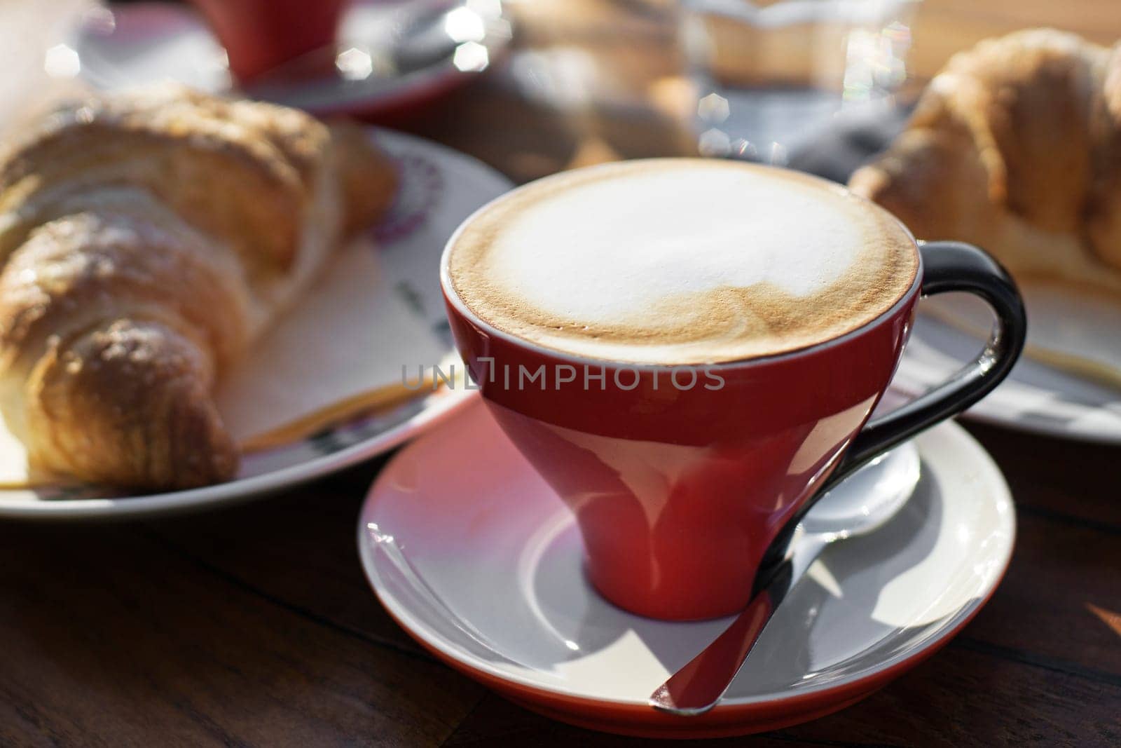 Coffee cup of cappuccino with croissant on wooden table.
