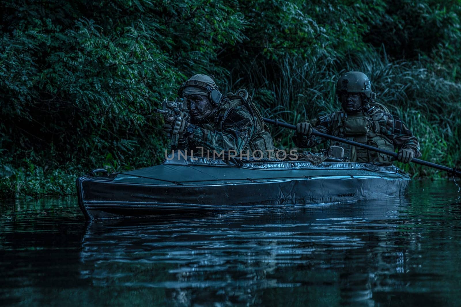 Special forces men with painted faces in camouflage uniforms paddling army kayak. Boat moving calmly across the river, diversionary mission, twilight