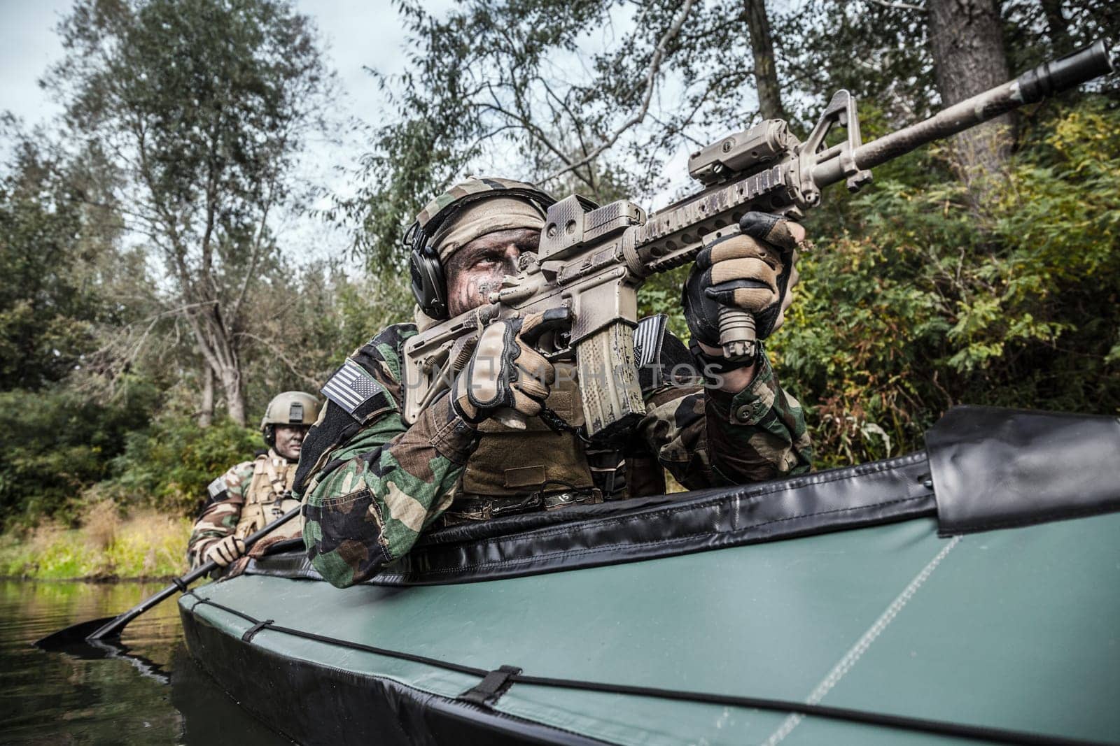 Special forces men with painted faces in camouflage uniforms paddling army kayak. Boat moving across the river, diversionary mission, front crop view