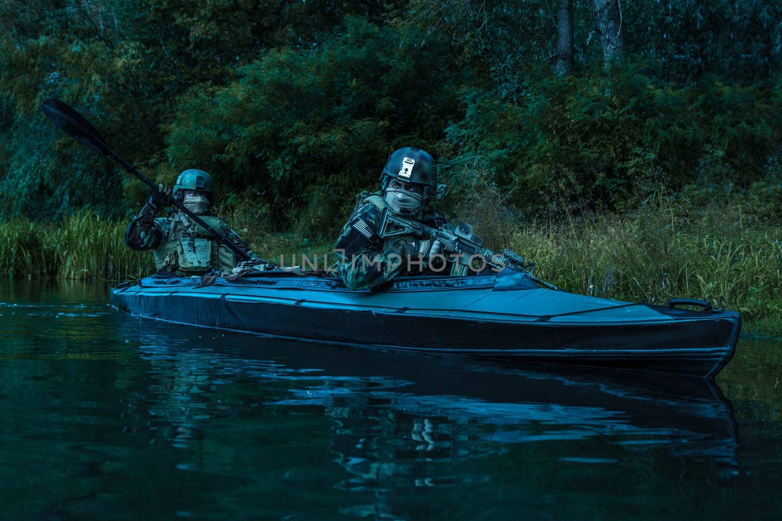 Special forces men with painted faces in camouflage uniforms paddling army kayak. Boat moving calmly across the river, diversionary mission, twilight