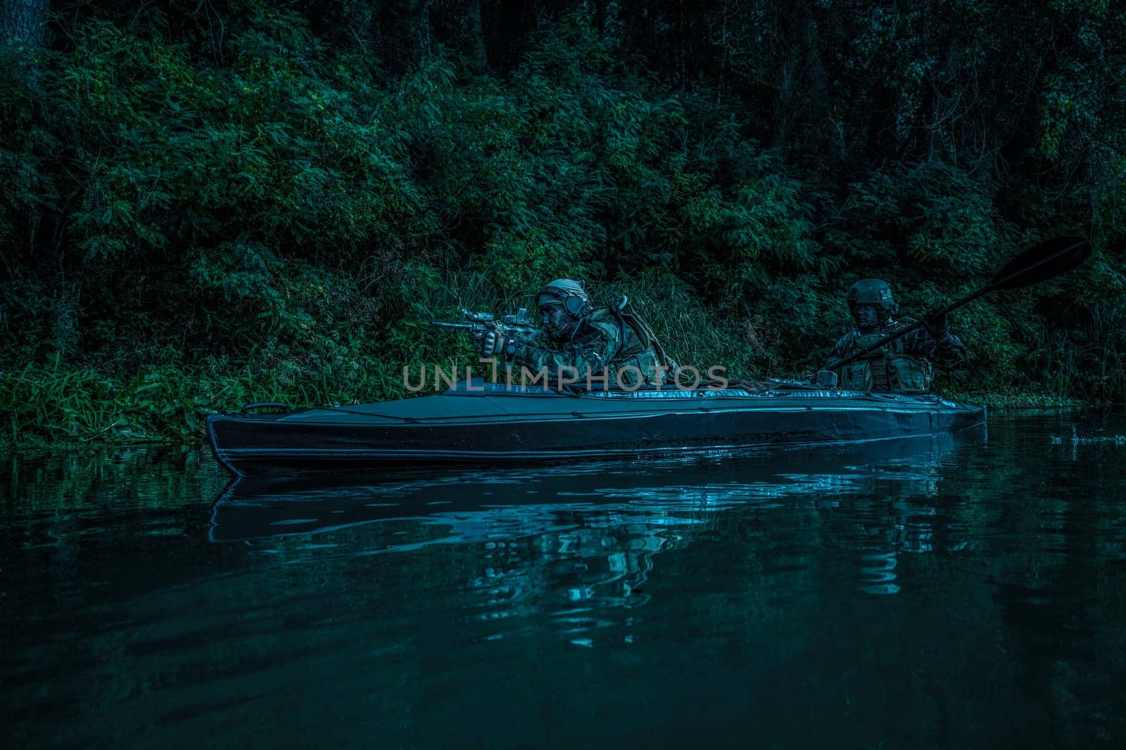 Special forces men with painted faces in camouflage uniforms paddling army kayak. Boat moving calmly across the river, diversionary mission, twilight