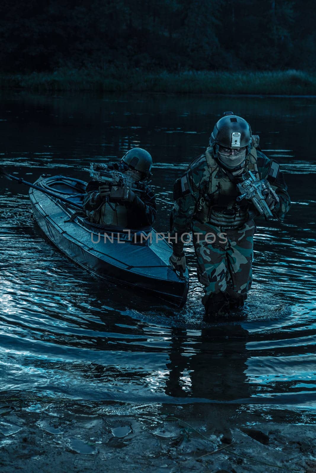 Covert landing. Pair of armed operators with painted faces disembarking river coast from military kayak . Diversionary mission under cover of darkness