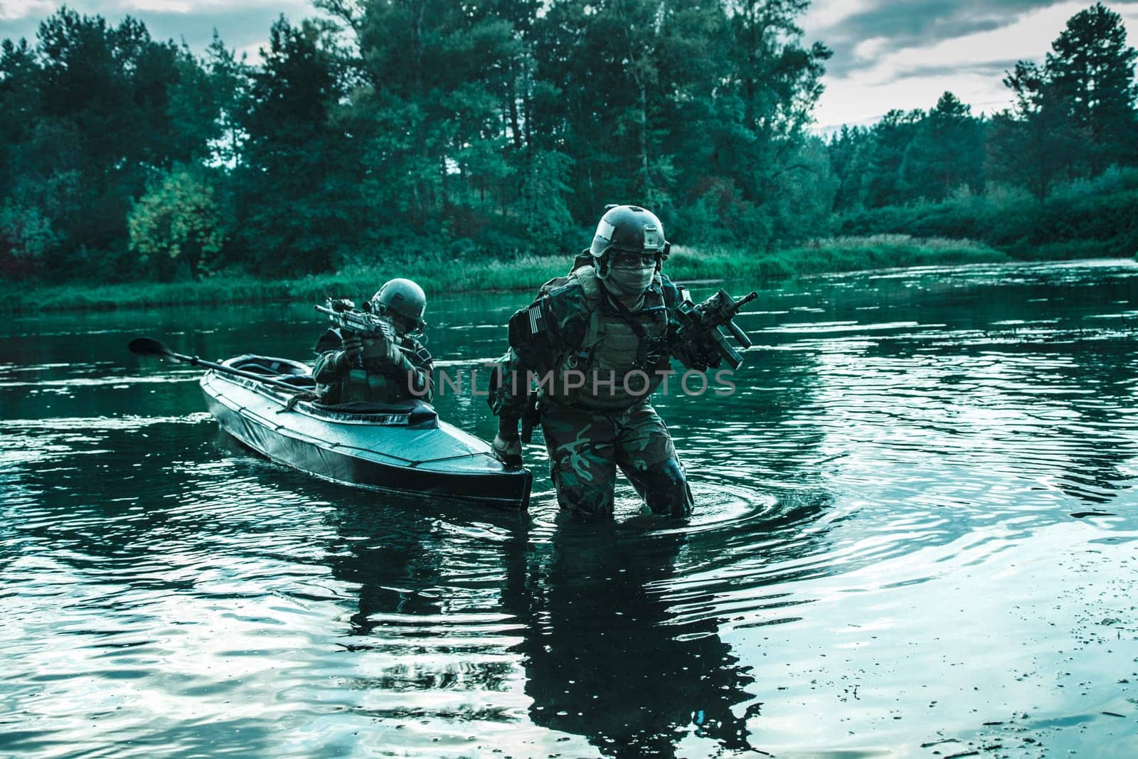 Covert landing. Pair of armed operators with painted faces disembarking from military kayak on river coast. Diversionary mission under cover of darkness