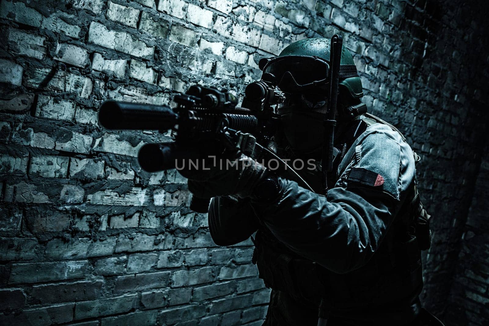 Special forces operator pointing weapon in the dark. Combat helmet, tactical radio system with folding antenna are on. Low key image