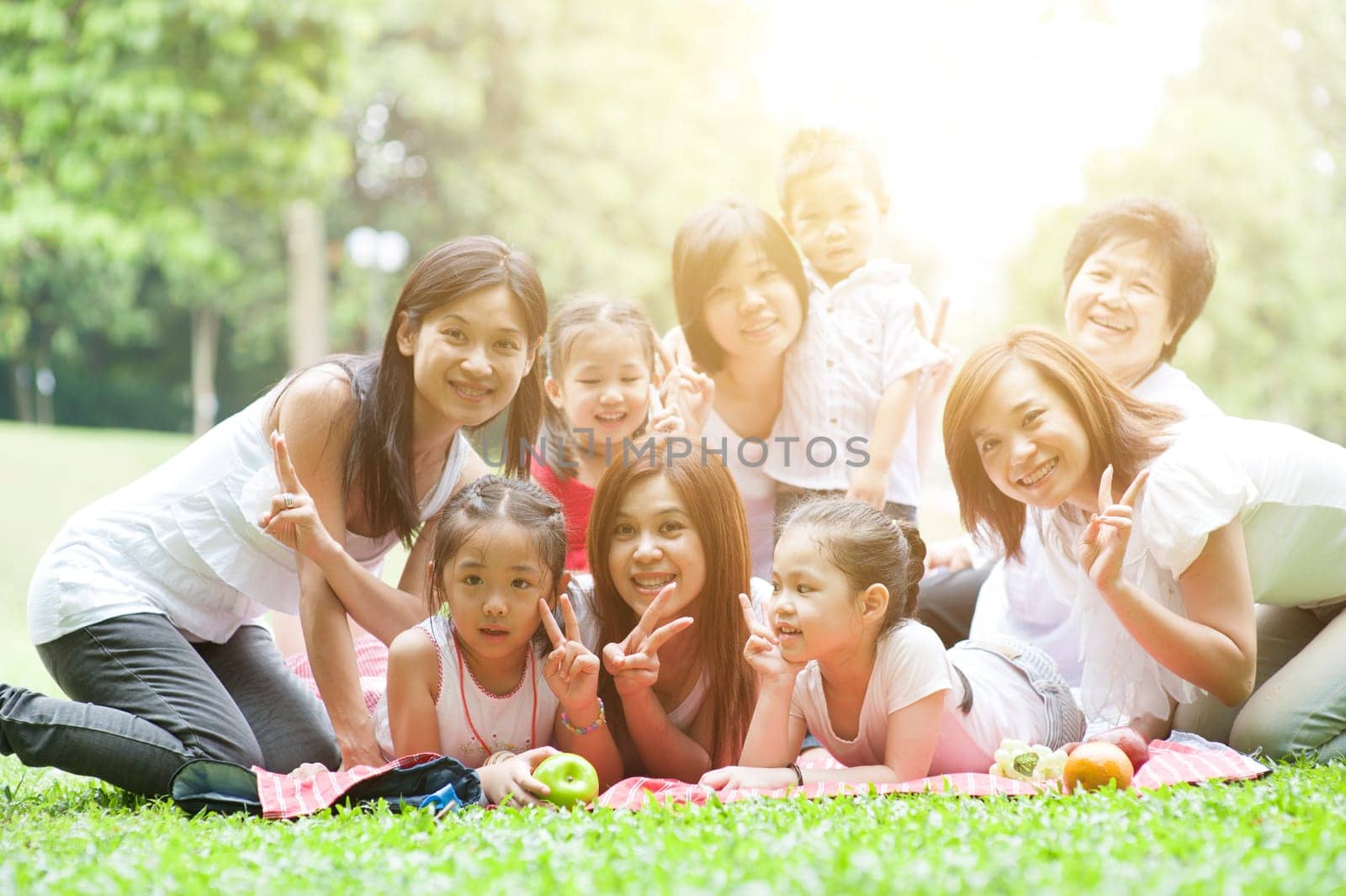 Cheerful Asian multi generations family portrait, grandparent, parents and children, outdoor nature park in morning with sun flare.