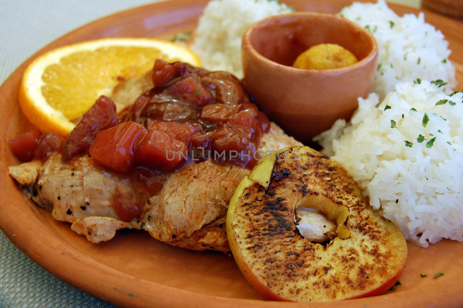 Turkey meat with different fruits and rice on earthenware plate.