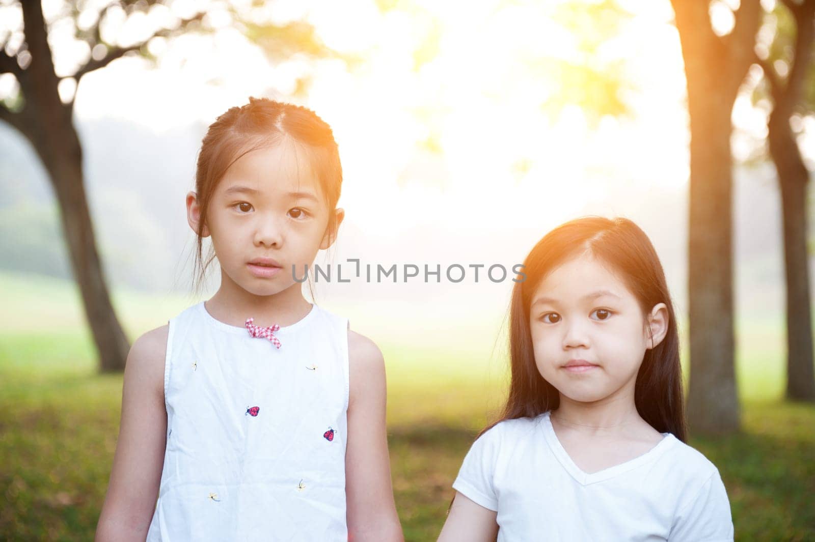 Portrait of Asian children at park. Little girls having fun outdoors. Morning sun flare background.