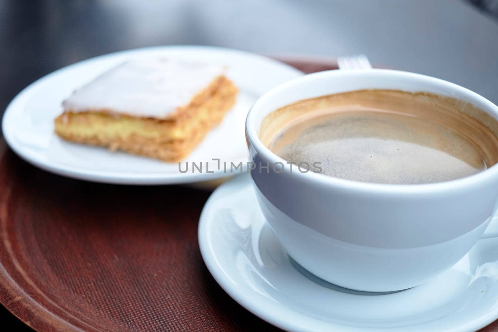 Shallow depth of field shot of coffee cup with mille feuille in the blurred background