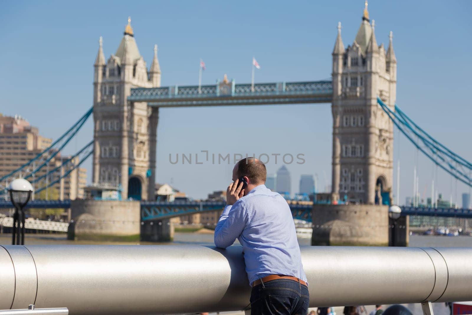 Businessman talking on mobile phone outdoor, looking at Tower Bridge in London city, UK.