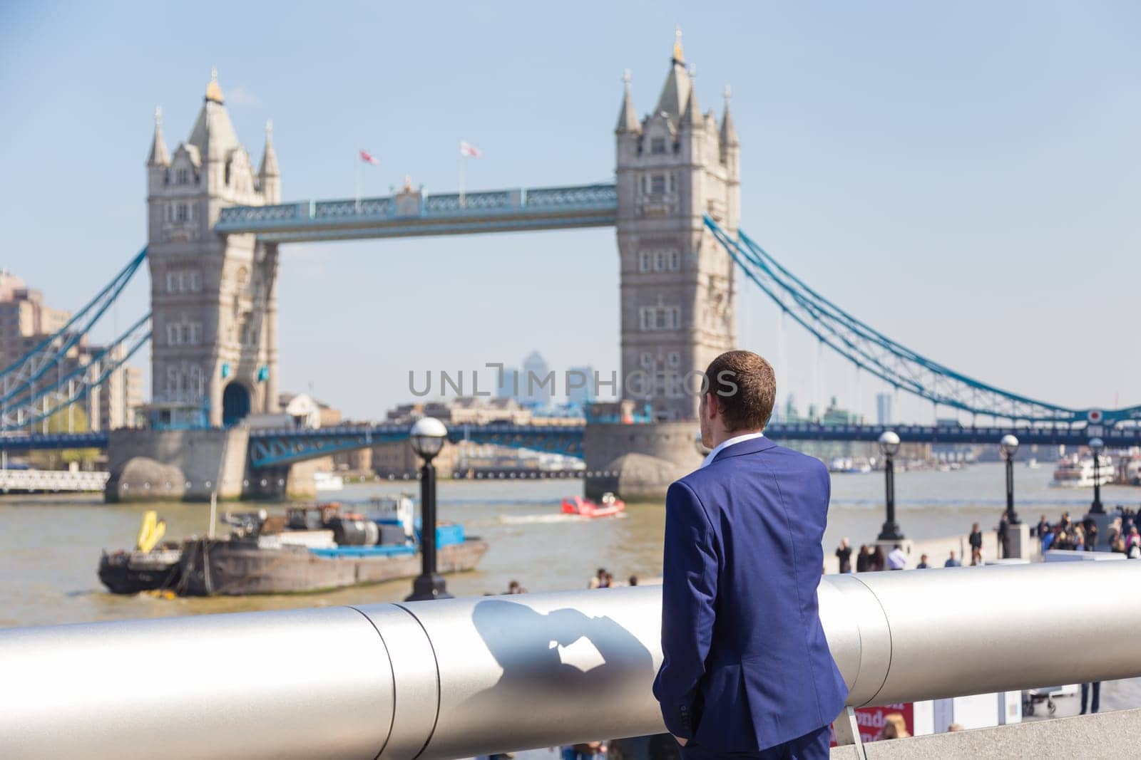 Businessman talking on mobile phone outdoor, looking at Tower Bridge in London city, UK.