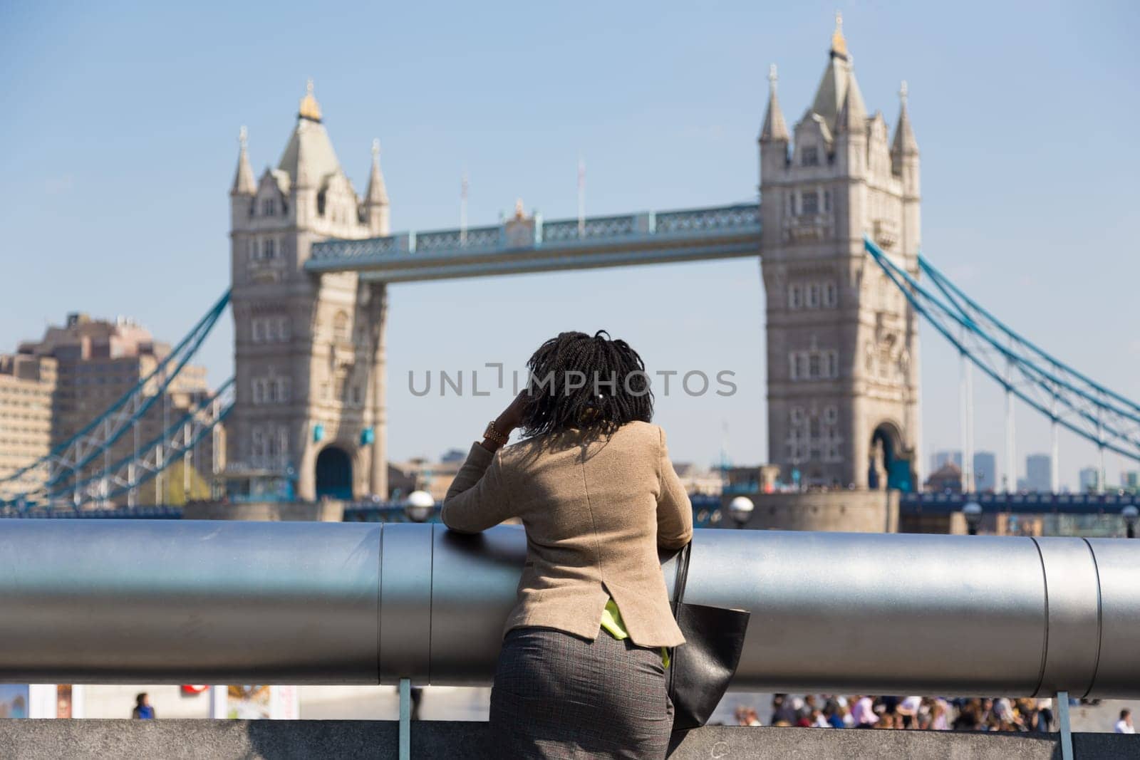Businesswoman talking on mobile phone outdoor, looking at Tower Bridge in London city, UK.