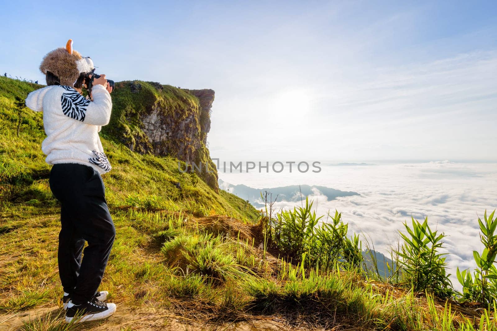 Asian hiker woman with digital camera photographing beautiful natural landscape of sky clouds and fog during sunrise in winter on mountain at Phu Chi Fa Forest Park, Chiang Rai Province, Thailand