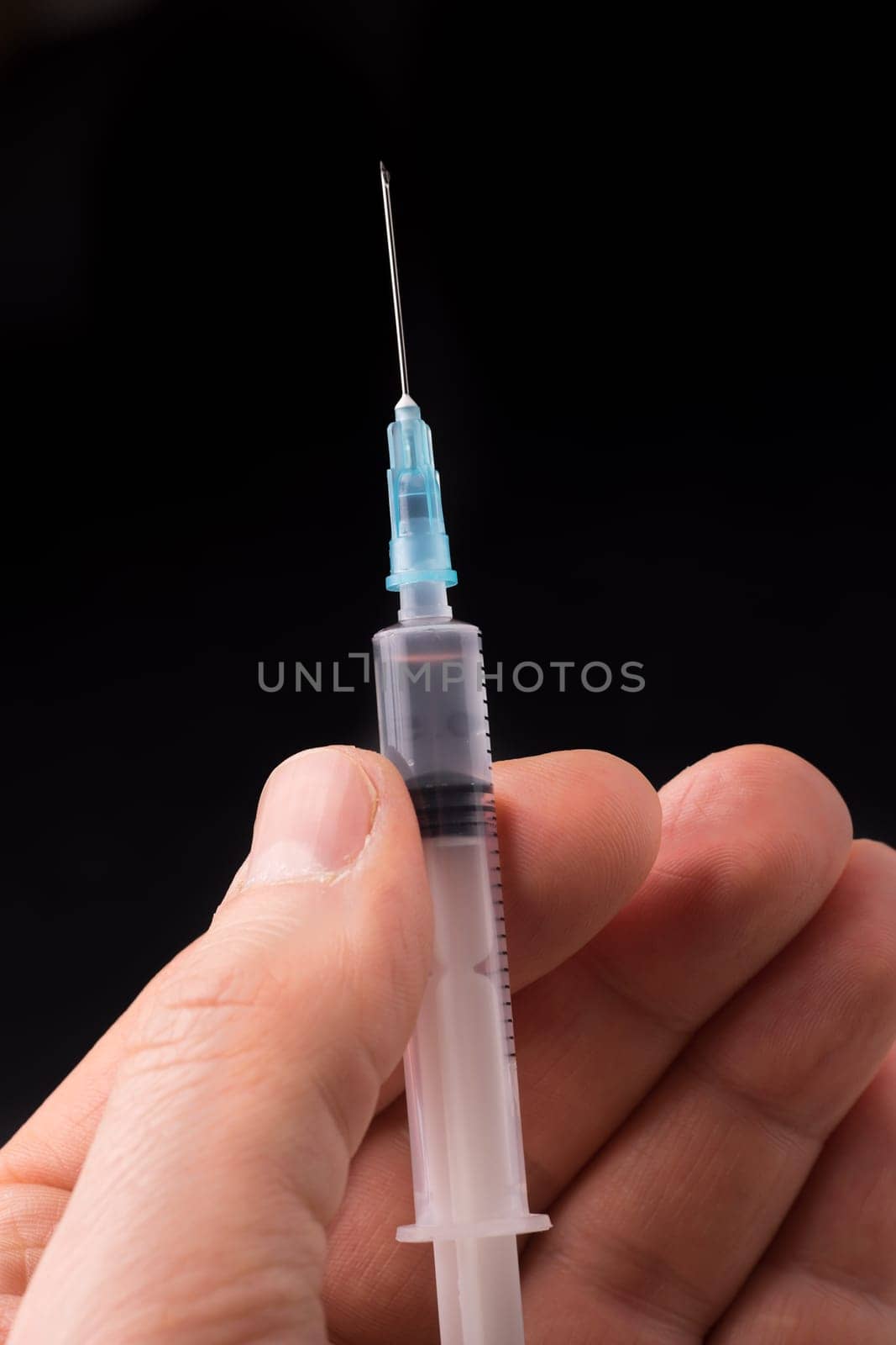 Hand holding a syringe, the syringe is filled with clear liquid and the photo is isolated on black background