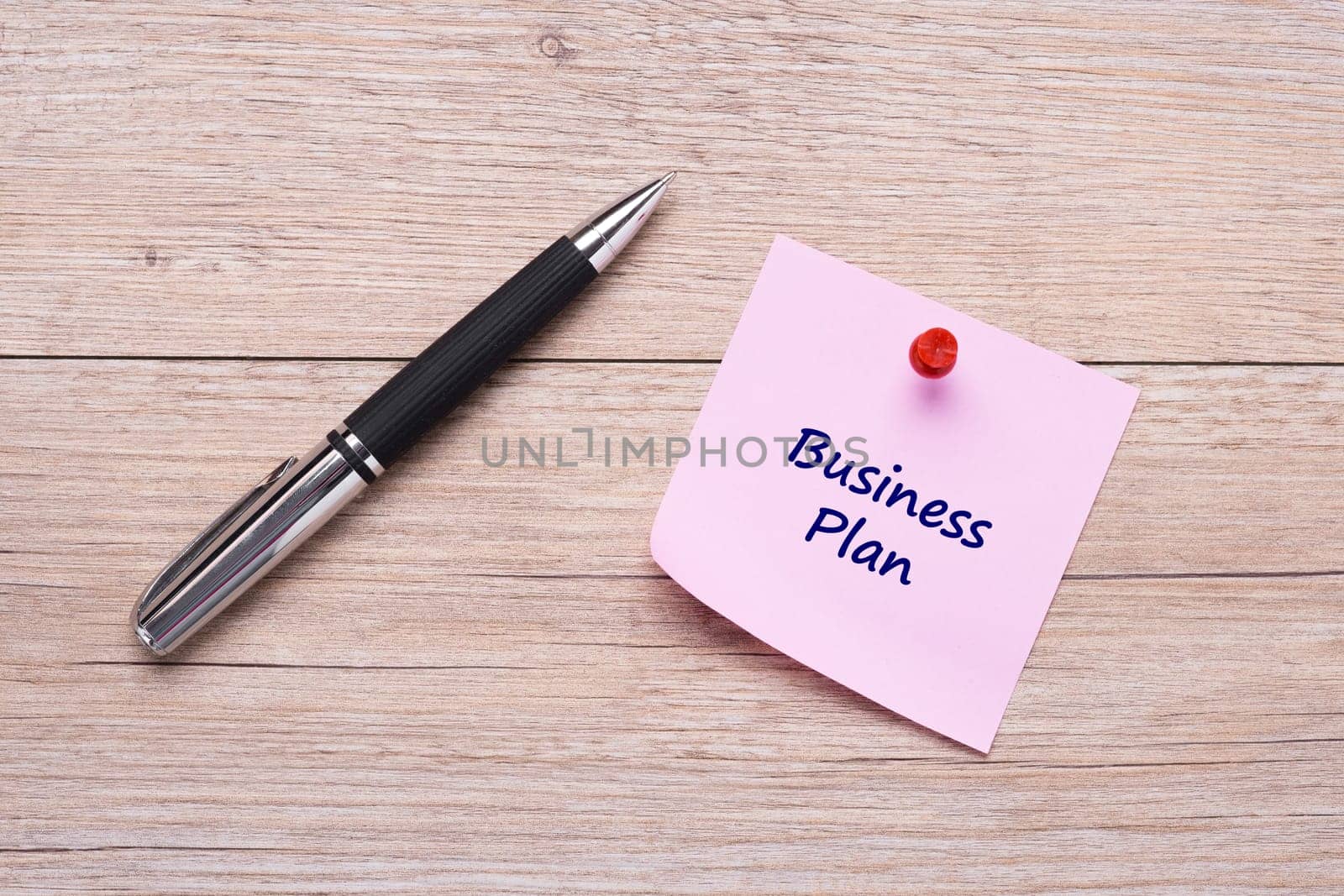 Handwriting Business Plan on pink sticky note with ballpoint pen