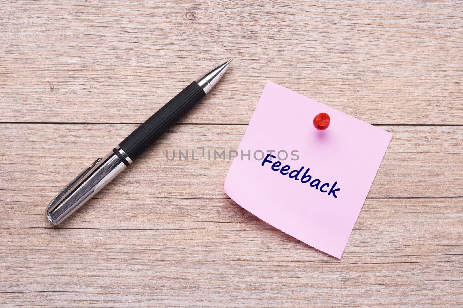 Concept feedback on pink sticky note with ballpoint pen on wood
