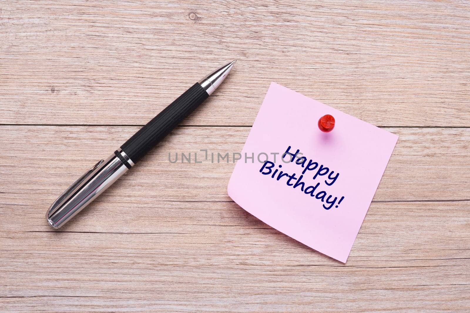 Concept Happy Birthday on pink sticky note with ballpoint pen on wood