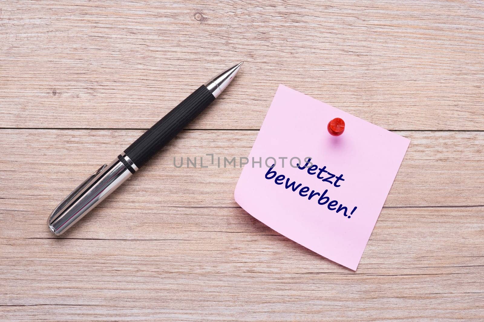 Apply text now on pink sticky note and ballpoint pen on wood