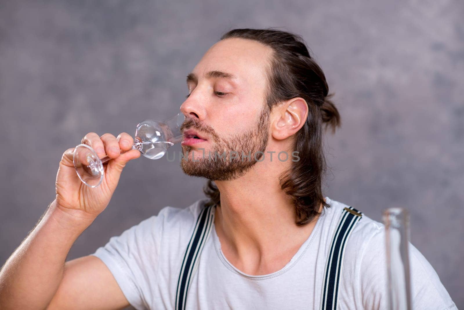 young man in front of gray background drinking clear spirit