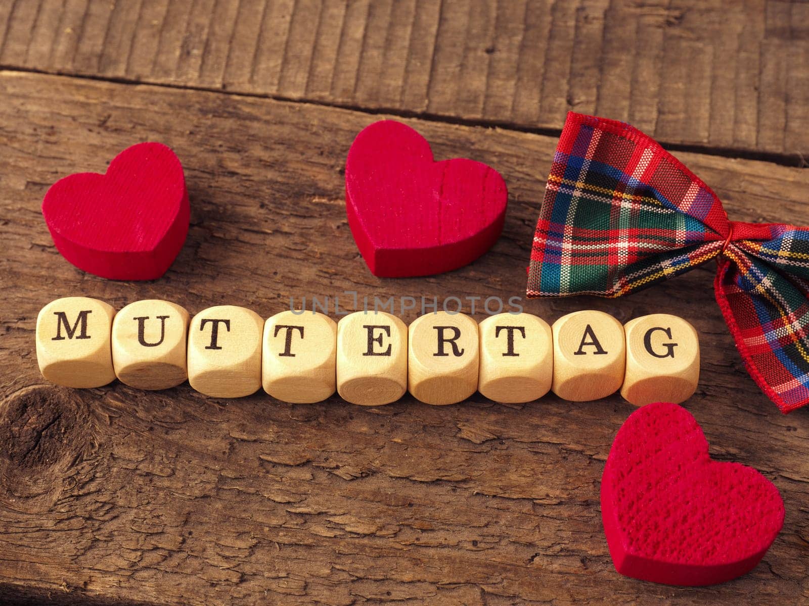Mothers Day background with the German word Mothersday on wooden dices, red heart shapes and bow decoration