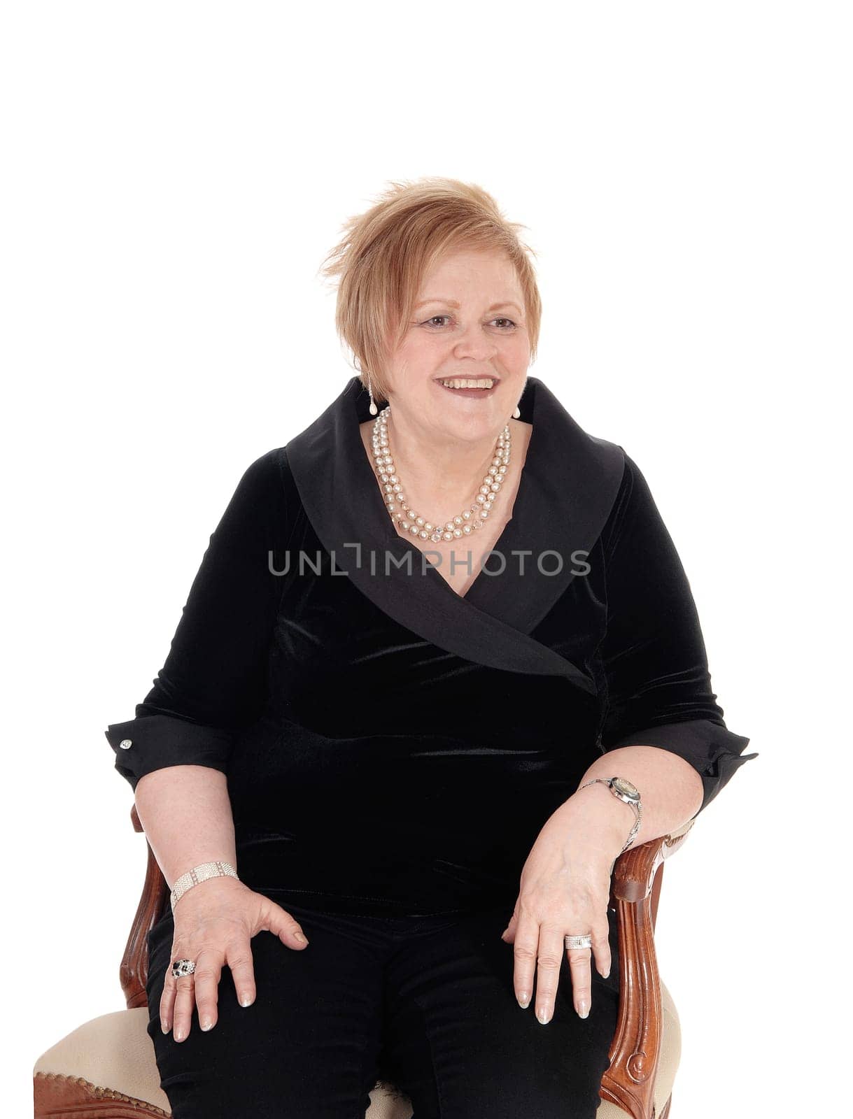 A happy smiling senior citizen woman in a black suit sitting in an old.armchair, relaxing, isolated for white background..