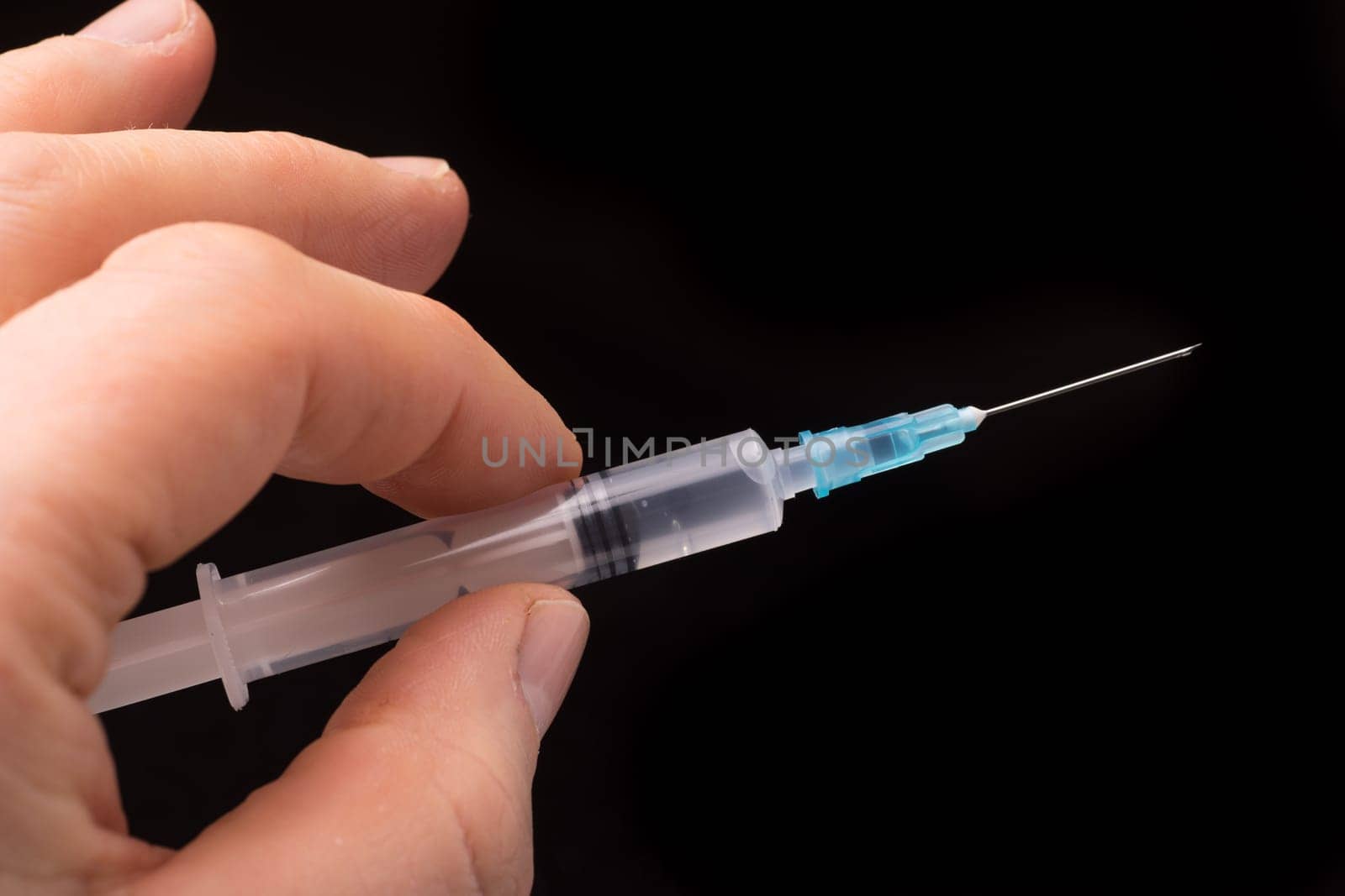 Hand holding a syringe, the syringe is filled with clear liquid and the photo is isolated on black background