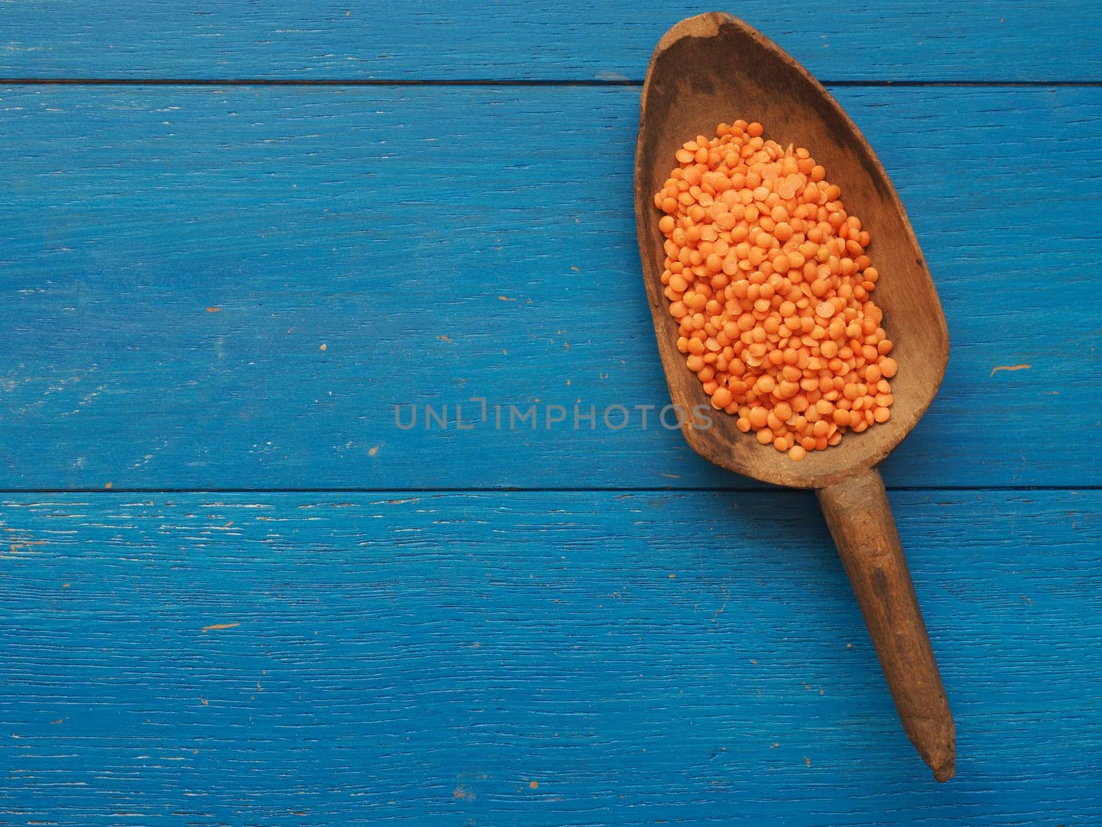 Rustic wooden spoon with red lentils on a blue wooden table
