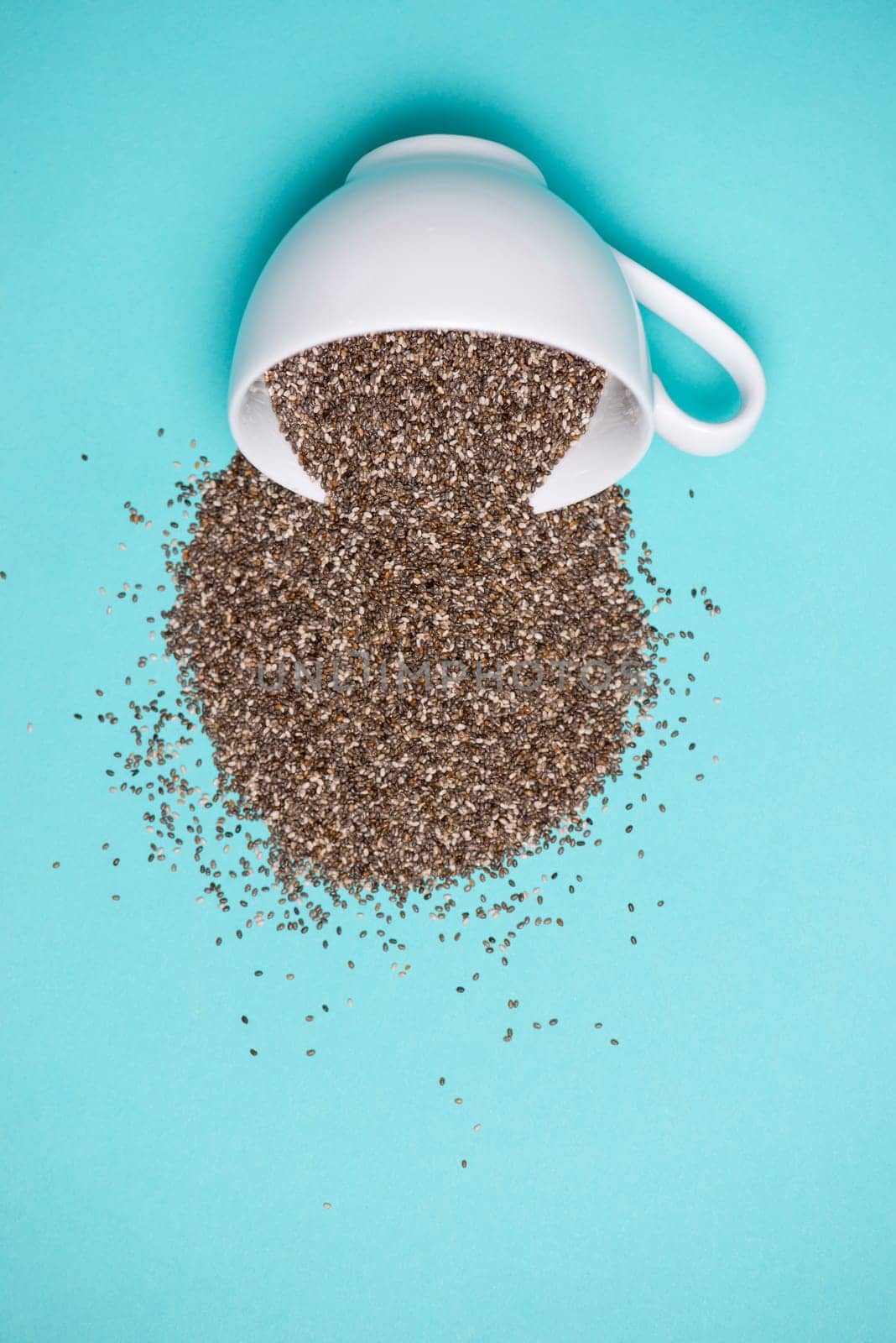 Nutritious chia seeds in cup on light blue background.