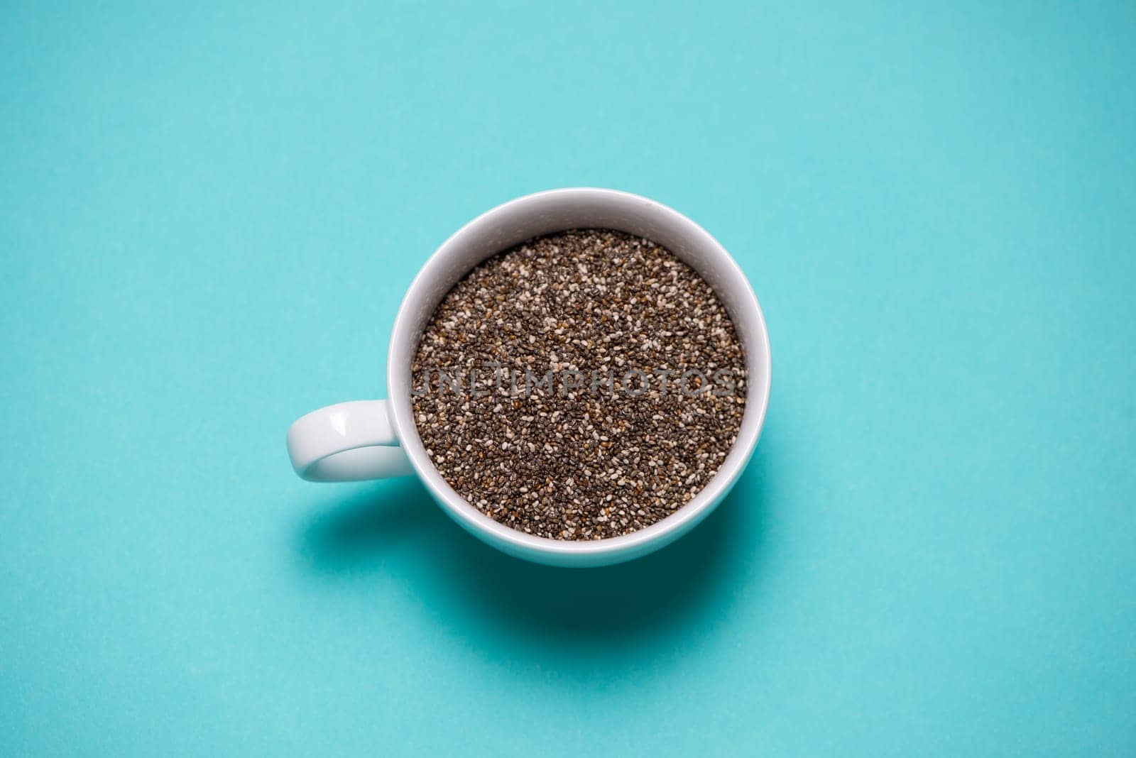 Nutritious chia seeds in cup on light blue background.