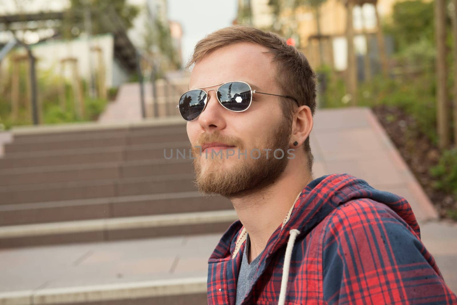 young bearded man with sunglasses in checkered shirt standing on stairs