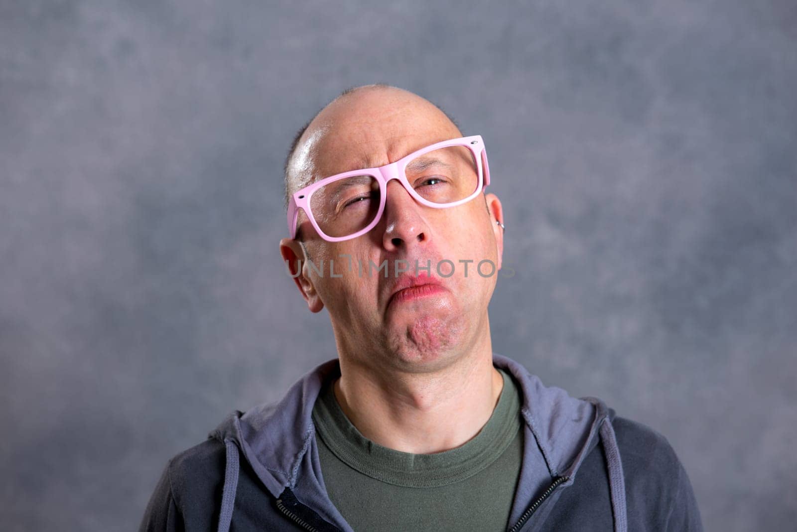 funny baldheaded man with pink glasses in front of gray background