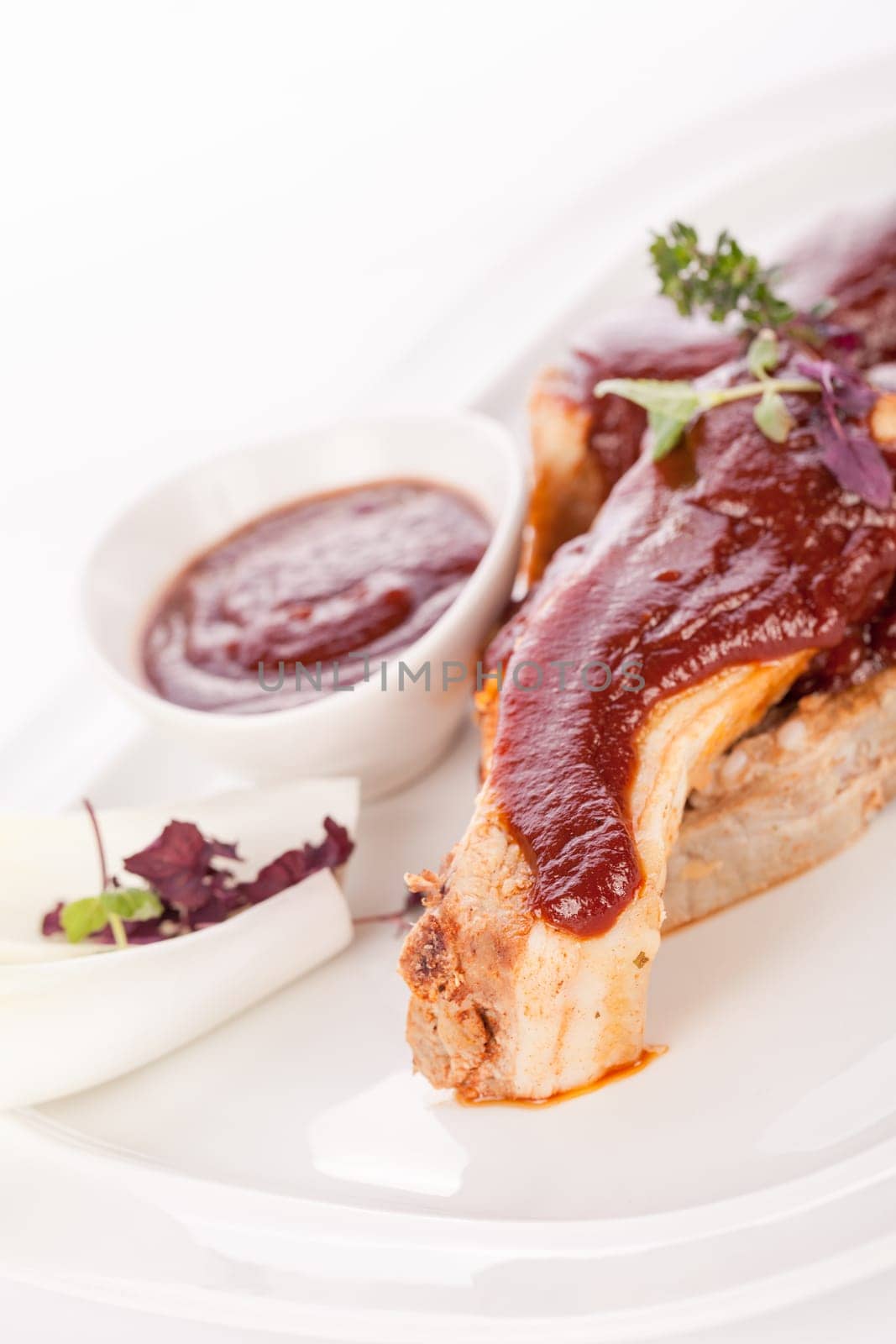 Grilled pork ribs Spareribs with barbecue sauce marinade and herb salad on a plate isolated against a white background