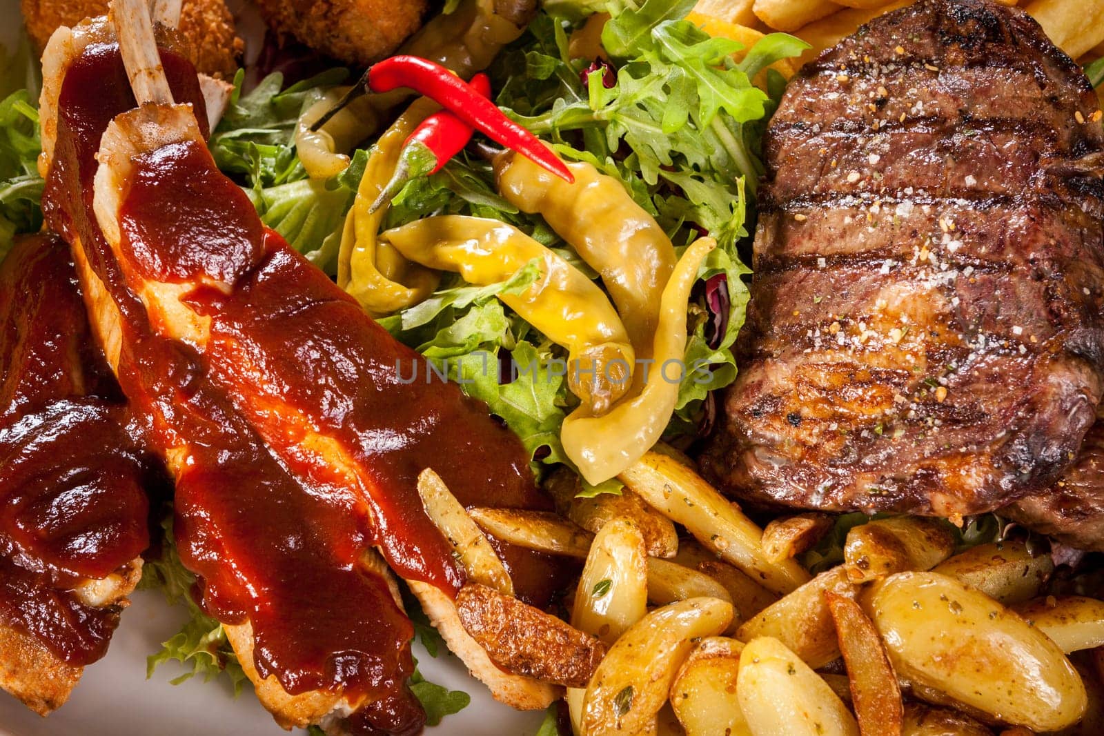 Huge barbecue plate with mixed meat and steaks on salad