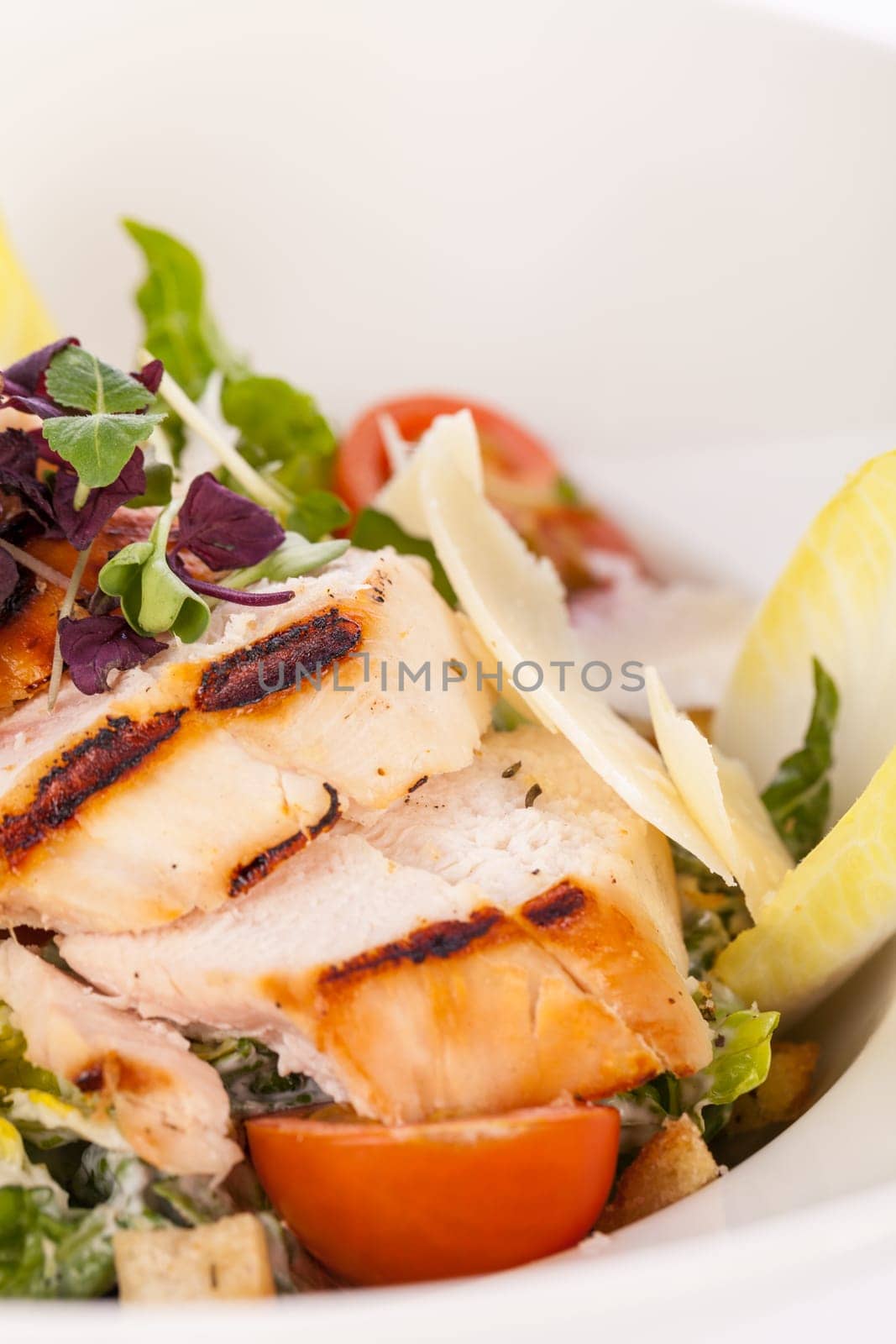 Fresh delicious caesarsalat with grilled chicken bust parmesan shards and croutons isolated against a white background