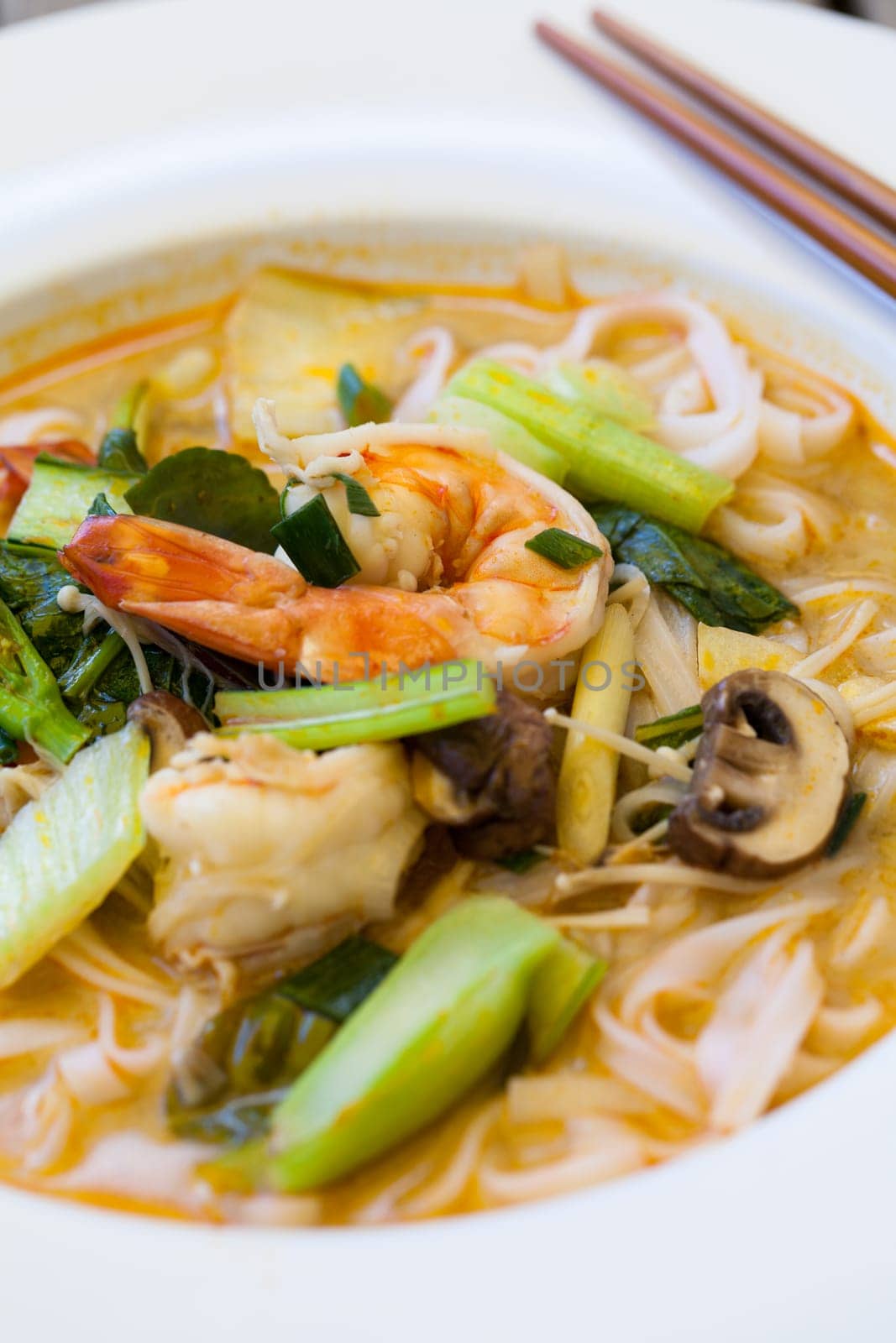 Bowl plate with freshly prepared Tom Yam soup with clanguste and coriander with chopsticks as close-up