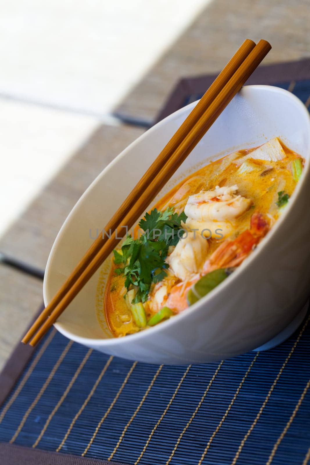 Bowl plate with freshly prepared Tom Yam soup with clanguste and coriander with chopsticks as close-up