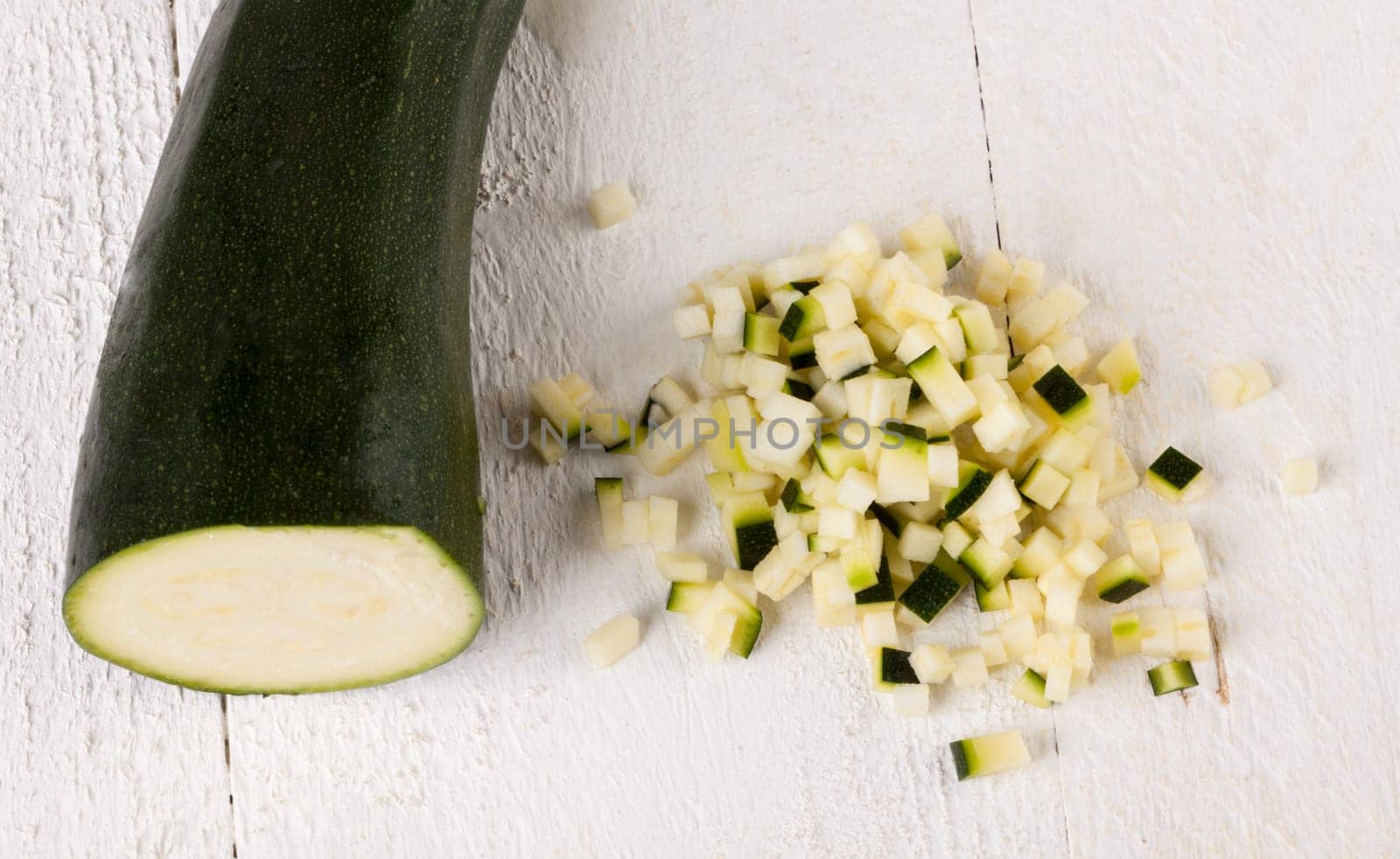 Fresh zucchini all in julienne strips and cut into brunoise cubes on a white hoözboard