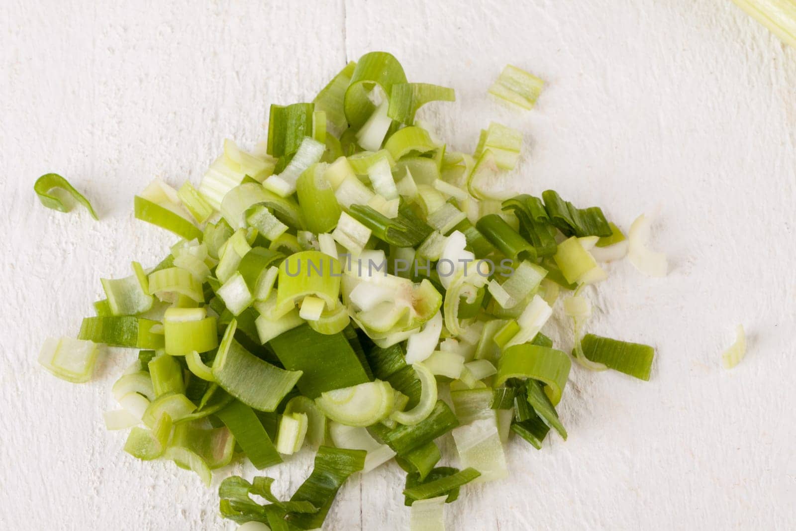 Leek spring onions with root as a whole and cut as a close-up on a white wooden board