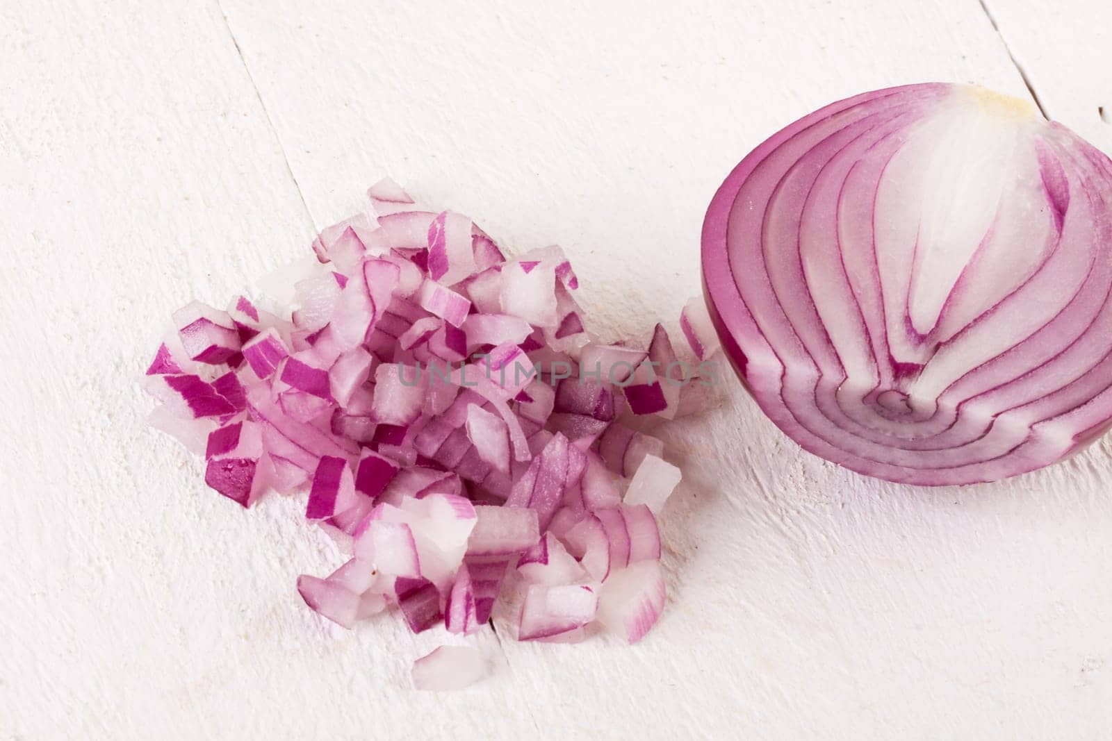 Red food onion whole and in small cubes Brunoise in a bowl on a white wooden board