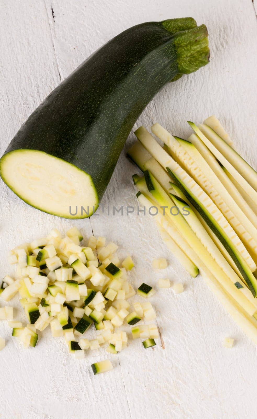 Fresh zucchini all in julienne strips and cut into brunoise cubes on a white hoözboard