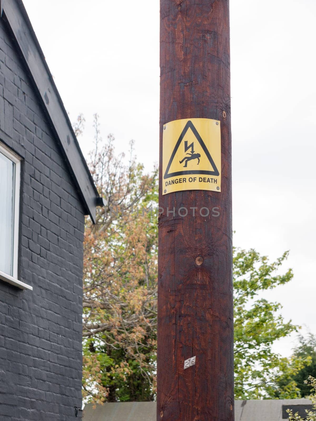 a yellow and black danger of death sign with electric bolt and man accident electrified on a wooden post outside home on street wires safety caution