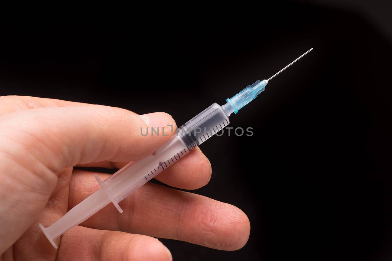 Hand holding a syringe, the syringe is filled with clear liquid and the photo is isolated on black background