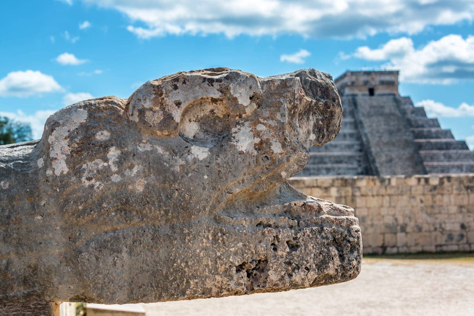 Stone snake head in Chichen Itza, Mexico with the Pyramid of Kukulcan in the background